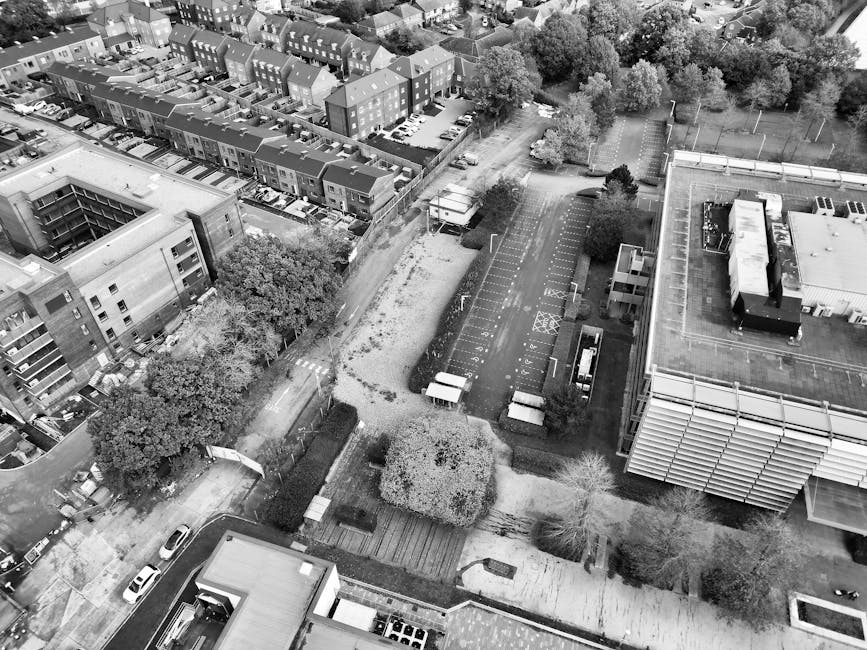 An aerial black-and-white photograph of a residential area showing multiple multi-story apartment buildings and detached houses. The foreground features a row of small houses with sloped roofs, some w
